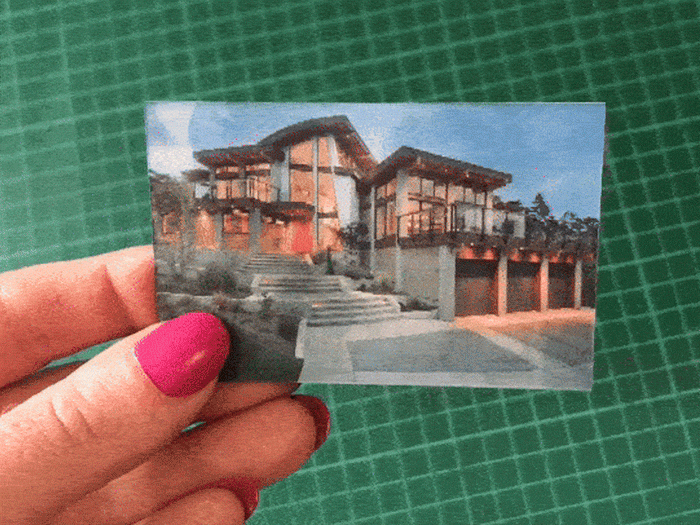 Hand holding a 3D lenticular card showing a modern house with large windows and garages.