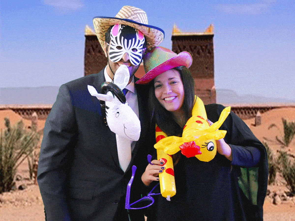 Two people in costumes with props, posing playfully in front of a desert-themed backdrop.