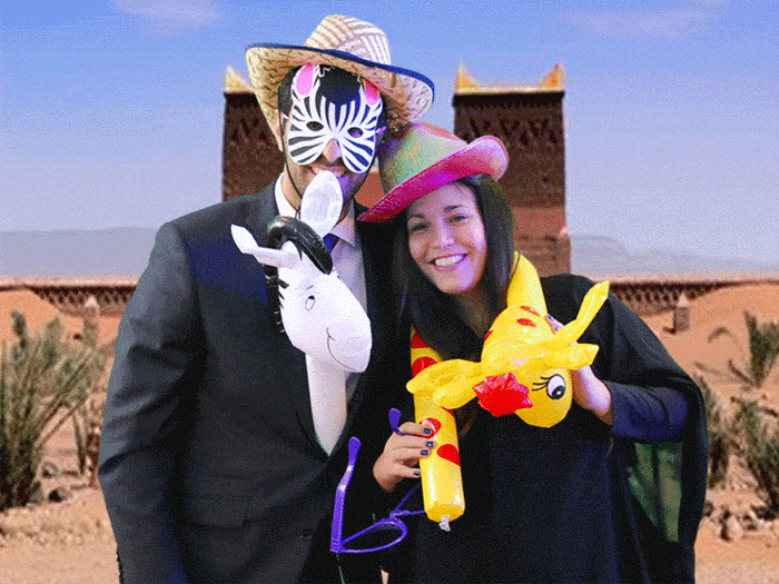Two people in costumes with props, posing playfully in front of a desert-themed backdrop.