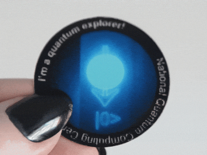 A round sticker shows a glowing qubit symbol and reads 